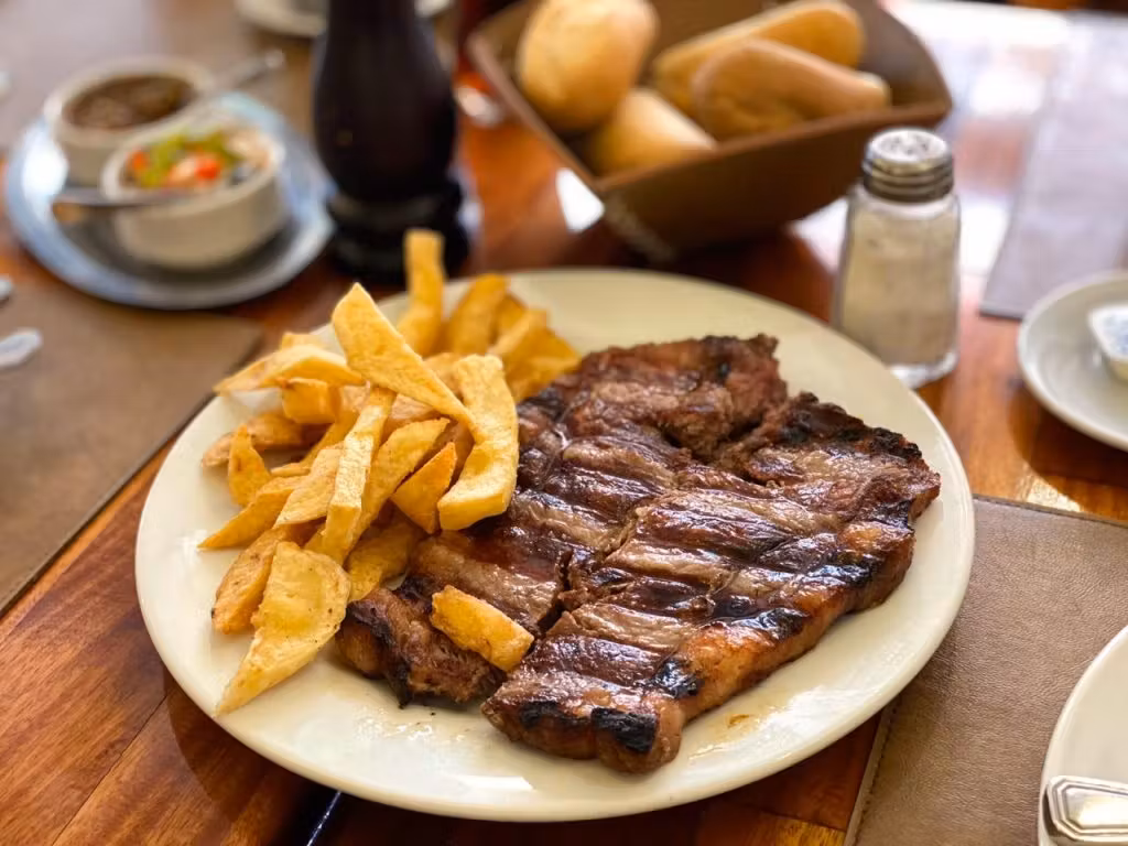 Foto em close de uma prato de filé com fritas e um saleiro ao fundo em um restaurante em Buenos Aires